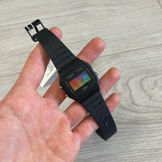Black Casio watch held in a hand on a light wooden surface