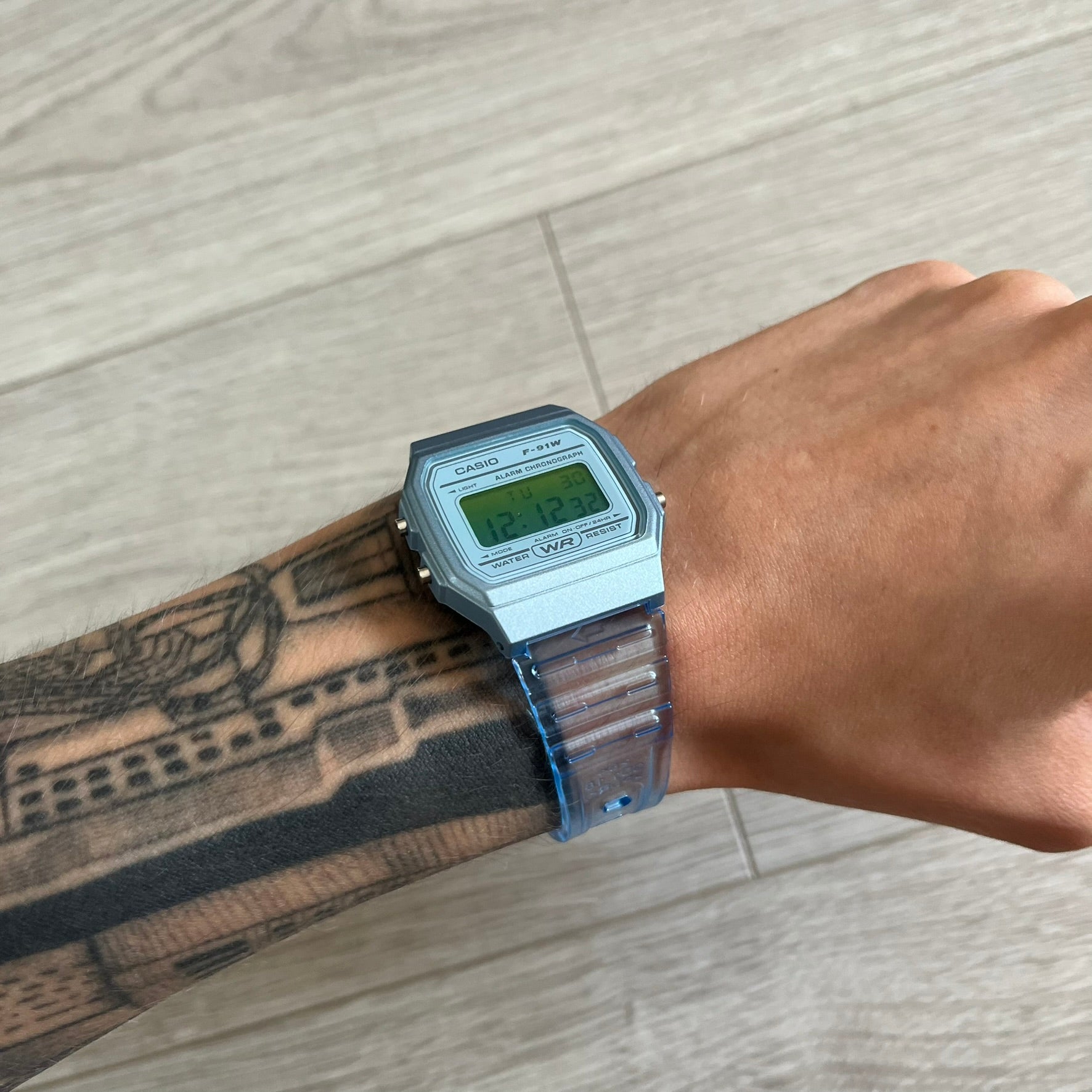 Digital watch on a wrist with tattoos against a wooden floor background