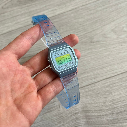 Digital watch with a clear blue strap held in a hand on a wooden surface