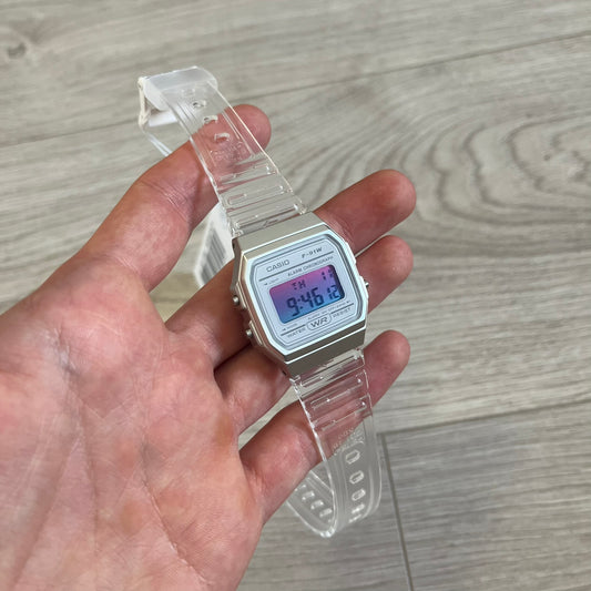 Digital watch with clear strap held in a hand on a wooden surface
