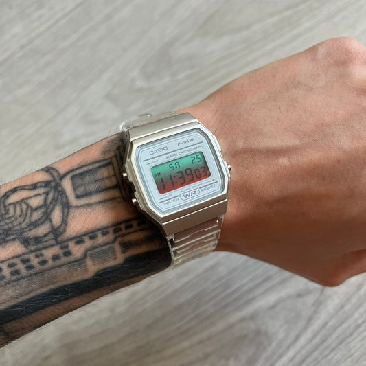 Casio digital watch on a wrist with tattoos, on a light wooden surface