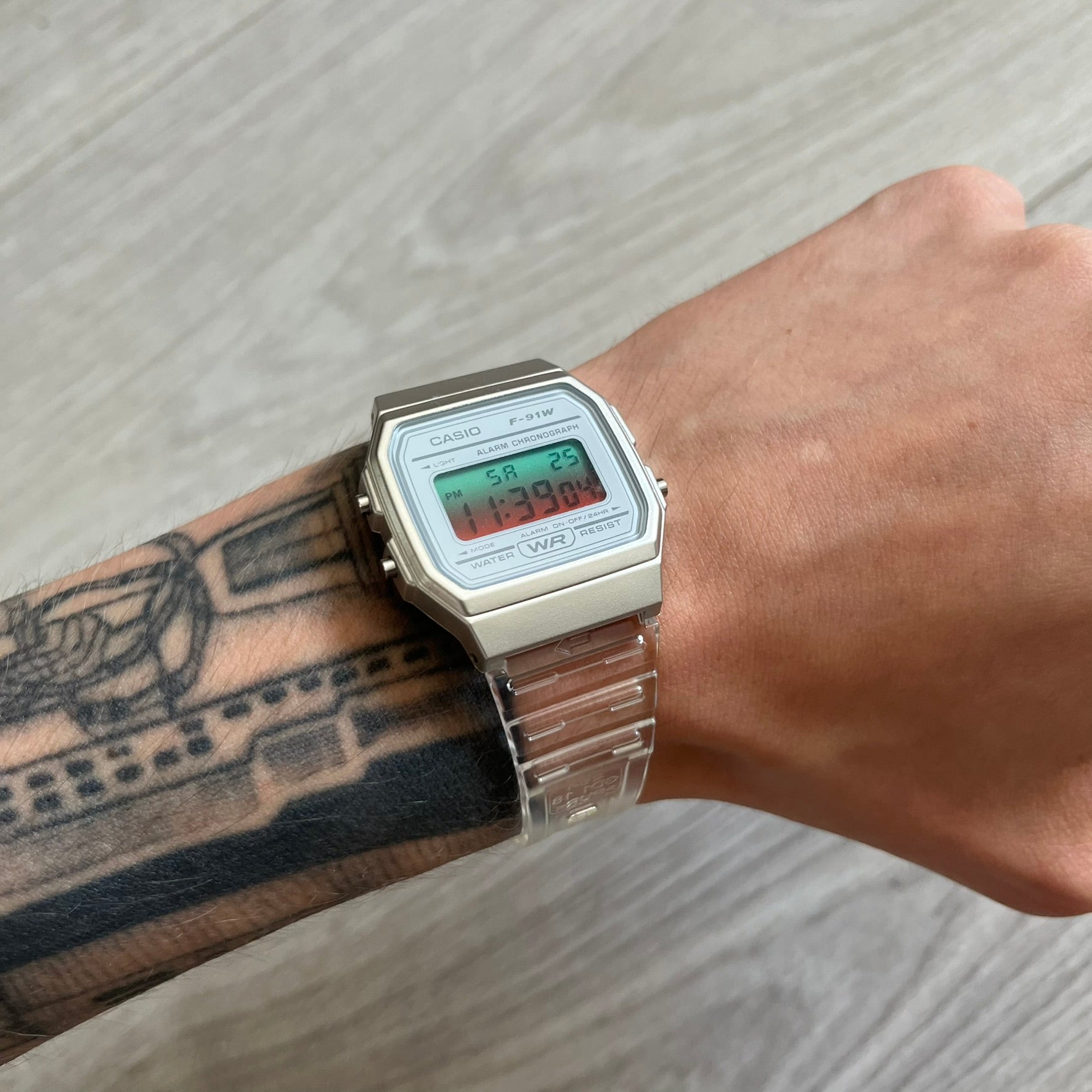Casio digital watch on a wrist with tattoos, on a light wooden surface