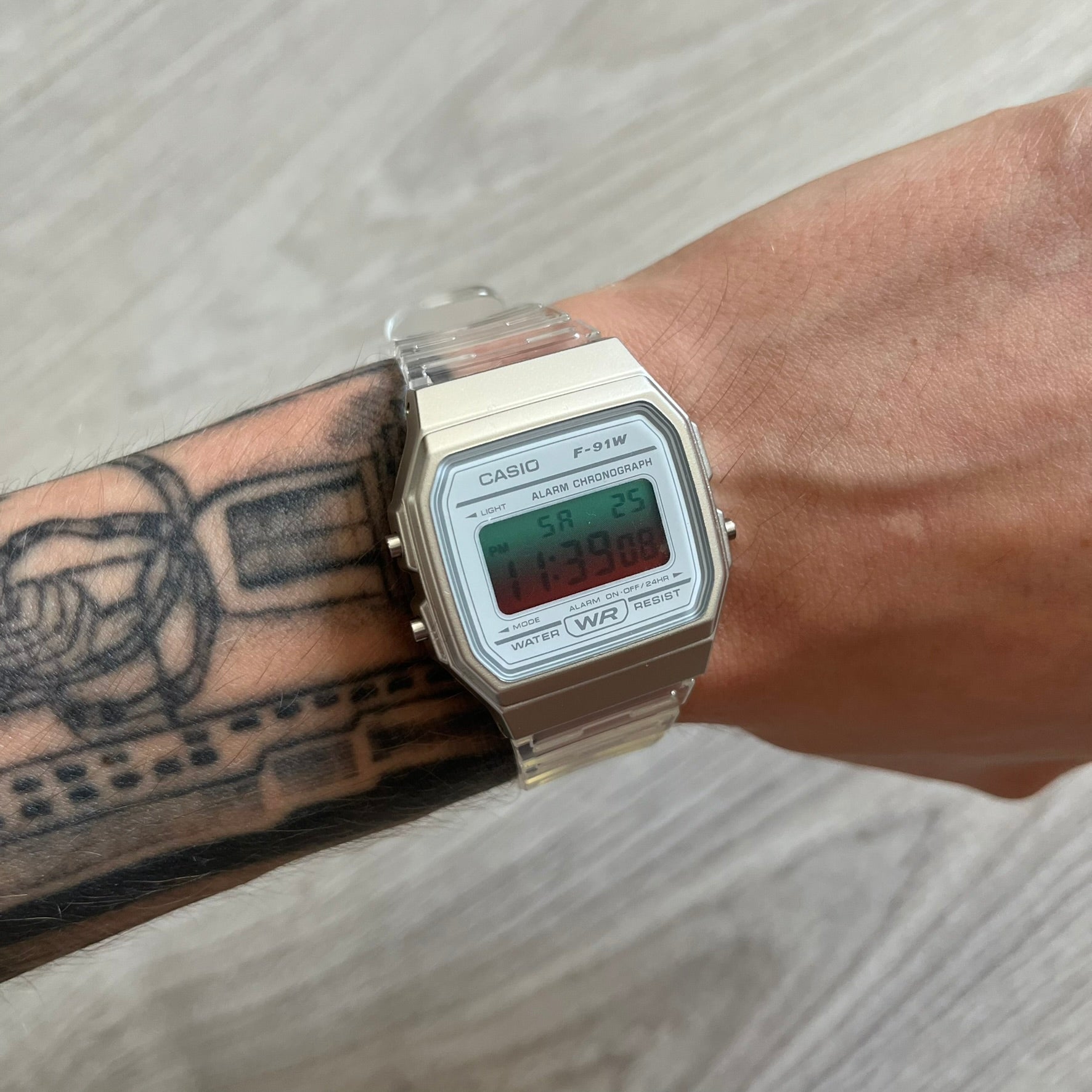 Casio digital watch on a wrist with tattoos, on a light wooden surface