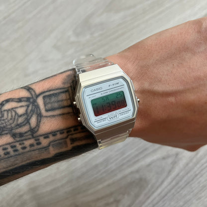 Casio digital watch on a wrist with tattoos, on a light wooden surface