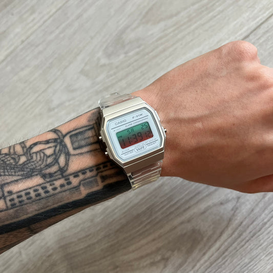 Digital watch on a wrist with tattoos, on a light wooden surface
