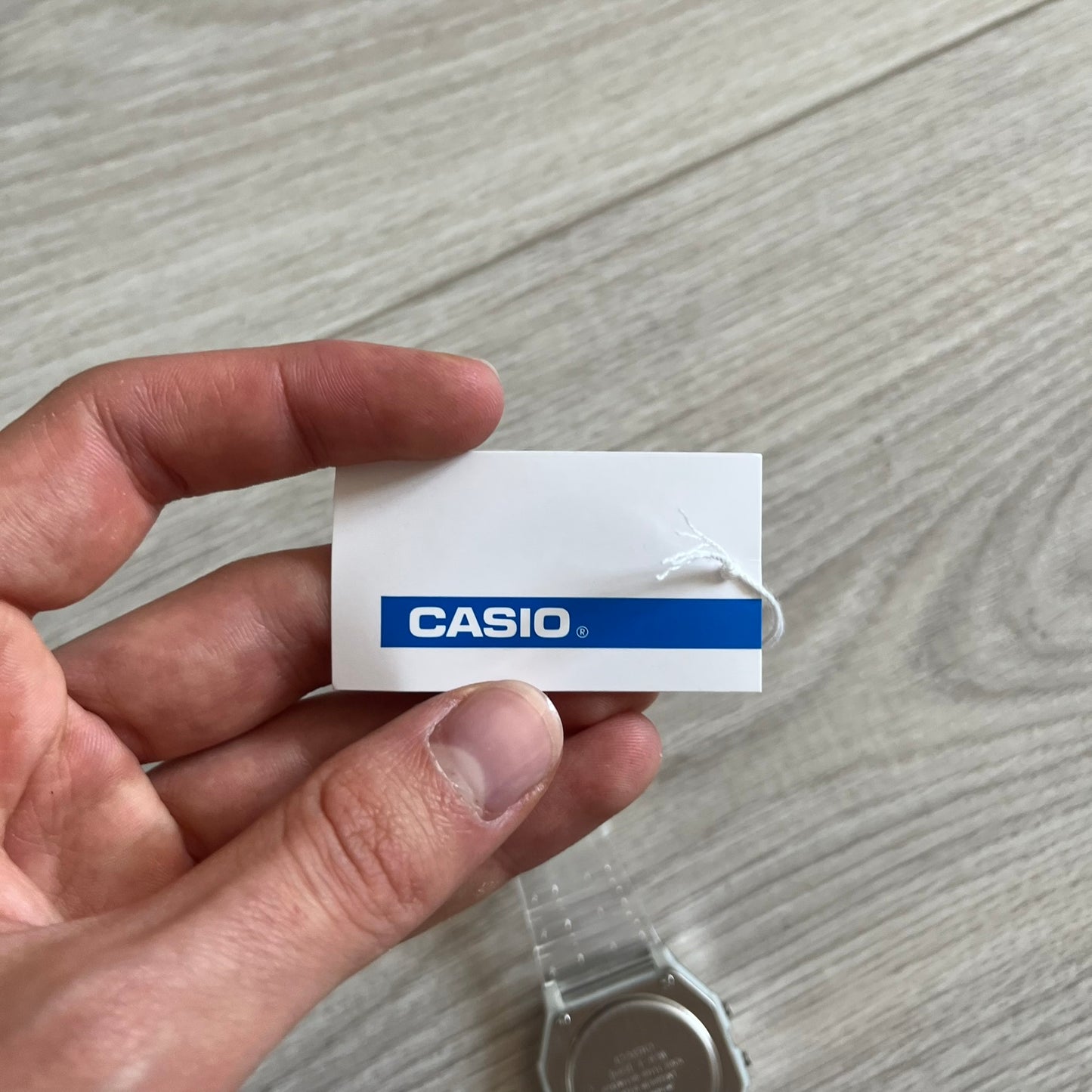 Hand holding a Casio watch tag on a wooden surface