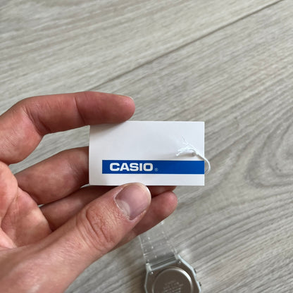 Hand holding a Casio watch tag on a wooden surface