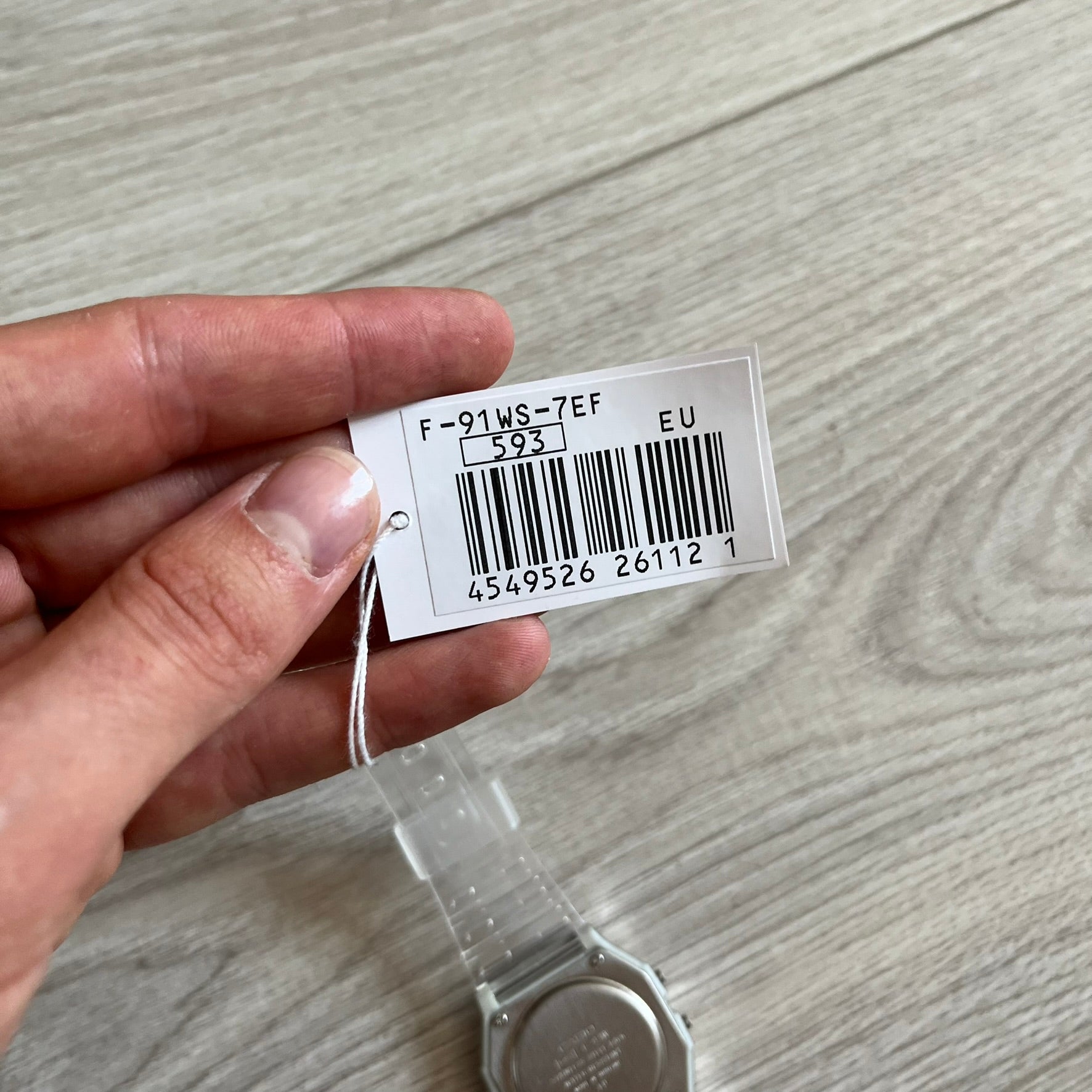 Hand holding a product tag with a barcode on a wooden surface