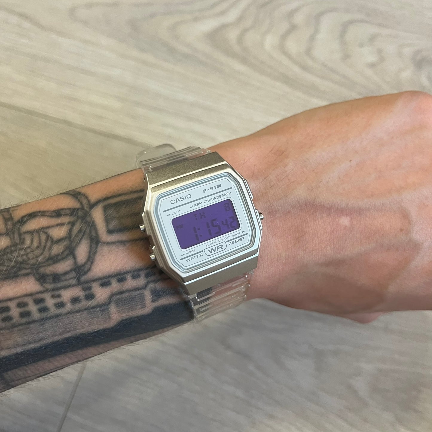 Casio digital watch on a wrist with tattoos against a wooden background