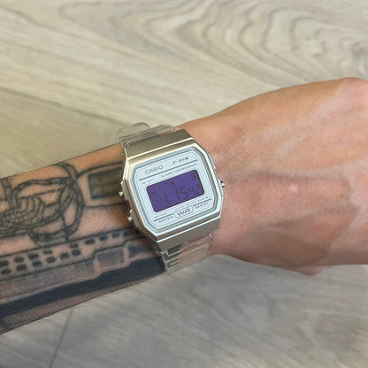 Casio digital watch on a wrist with tattoos against a wooden background