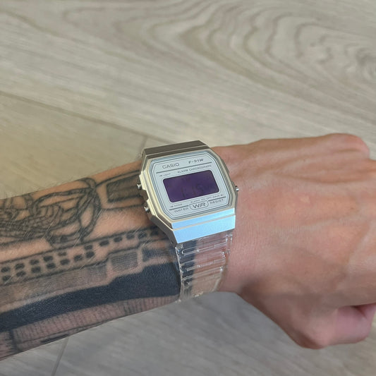 Casio digital watch on a wrist with tattoos, against a wooden surface background