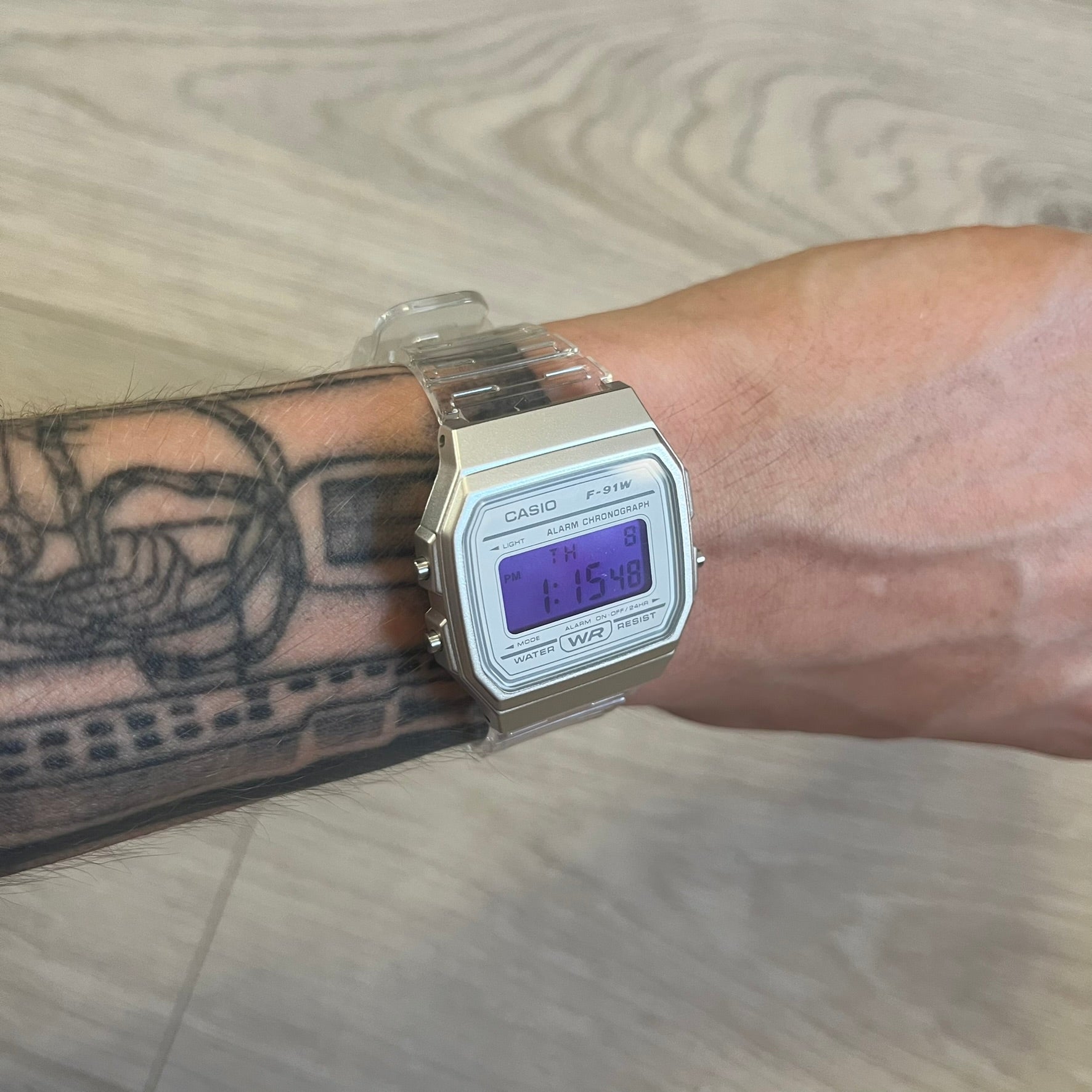 Casio digital watch on a wrist with tattoos, on a wooden floor background