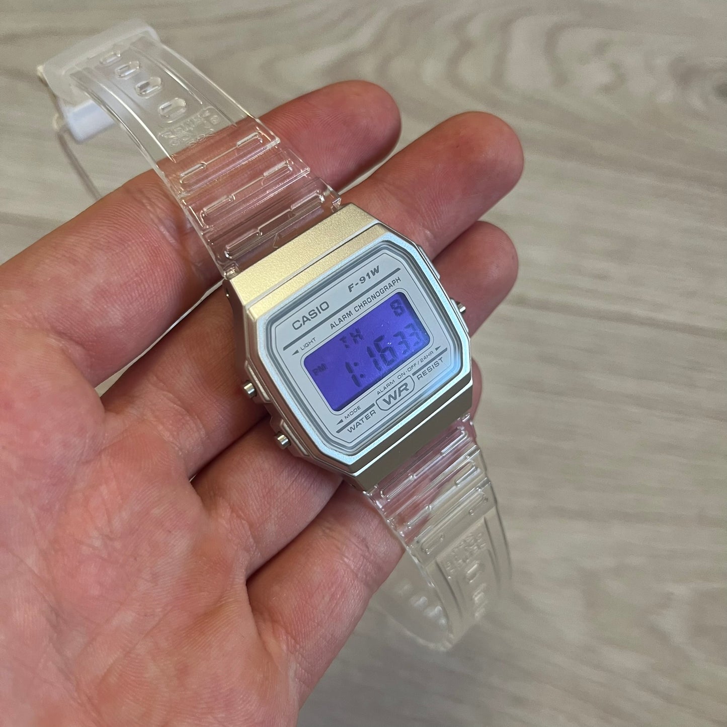 Digital Casio watch held in a hand with a light wood background