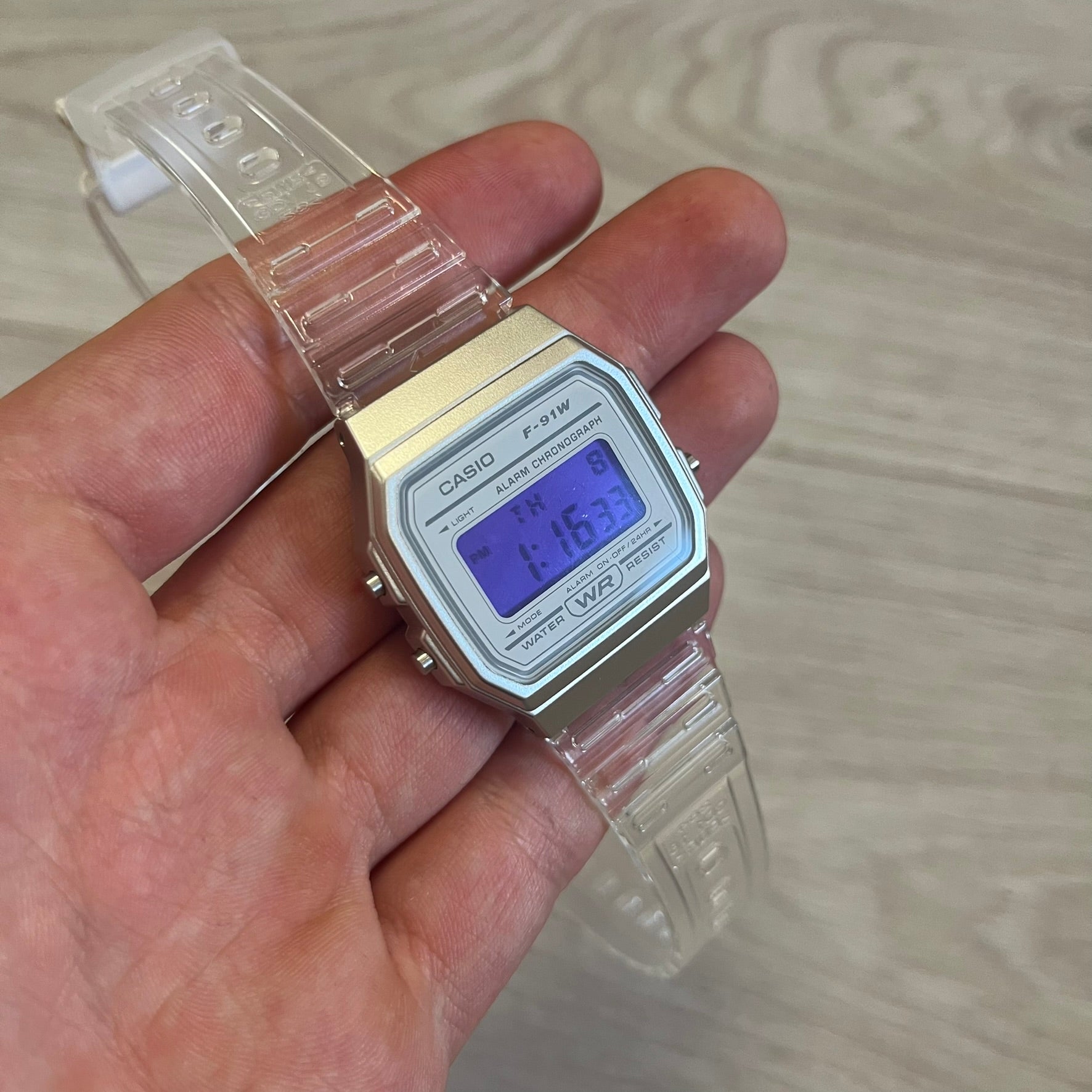 Digital Casio watch held in a hand with a light wood background