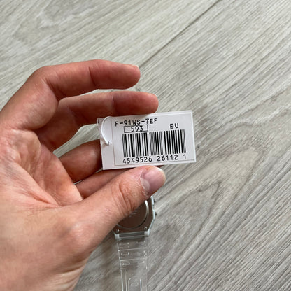 Hand holding a small white label with a barcode on a gray surface
