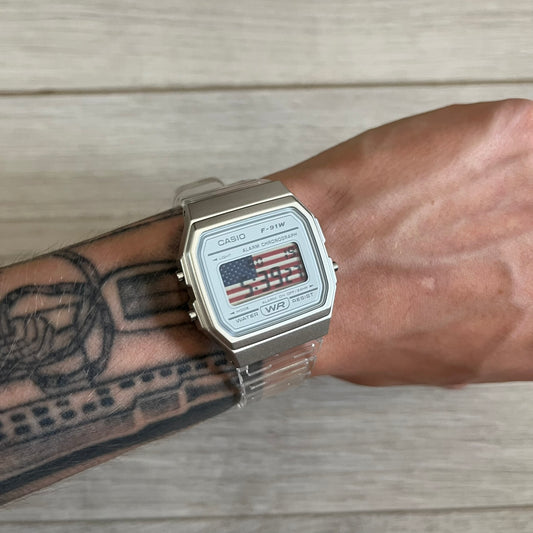 Casio watch with American flag design on a wrist with tattoos, wooden background