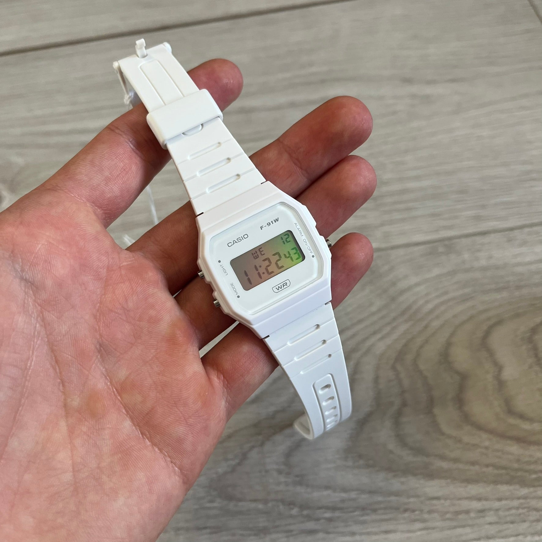 White digital watch held in a hand on a wooden surface