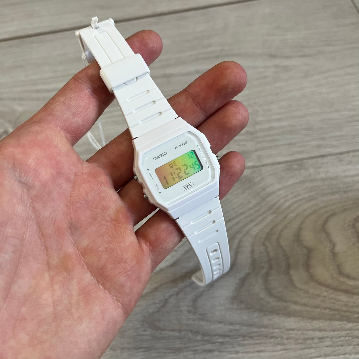White Casio digital watch held in a hand on a wooden surface
