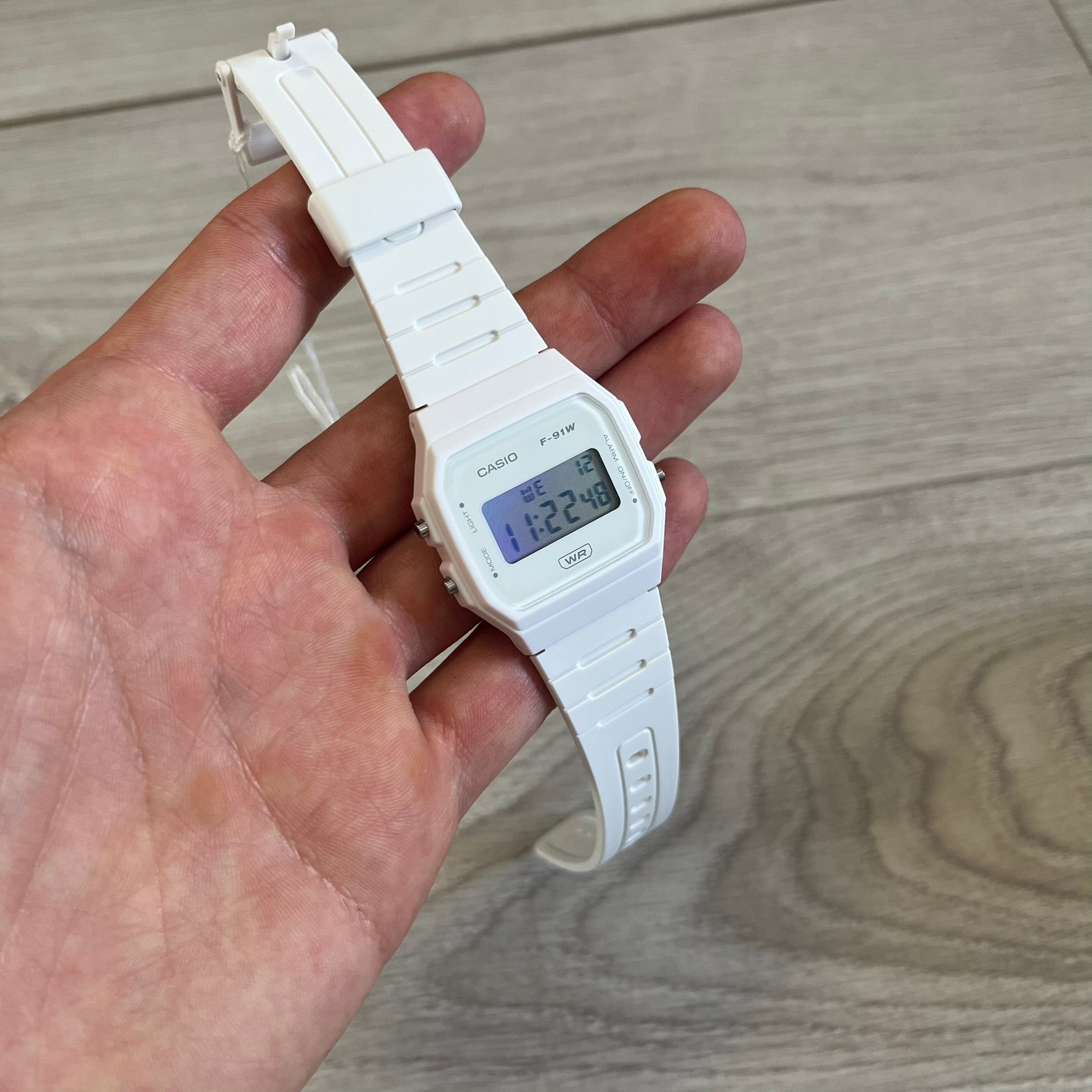 White digital watch held in a hand on a wooden surface