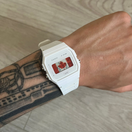White Casio watch on a wrist with a tattooed arm, on a neutral background