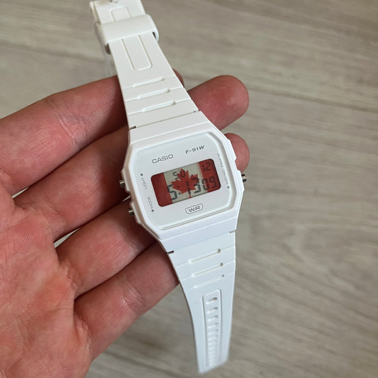 White Casio digital watch held in a hand on a light wooden surface