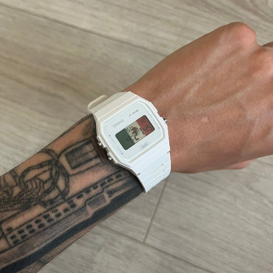 White digital watch on a wrist with tattoos, against a wooden floor background