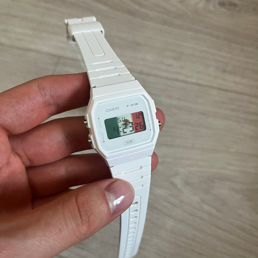 White Casio digital watch held in a hand on a light wooden surface