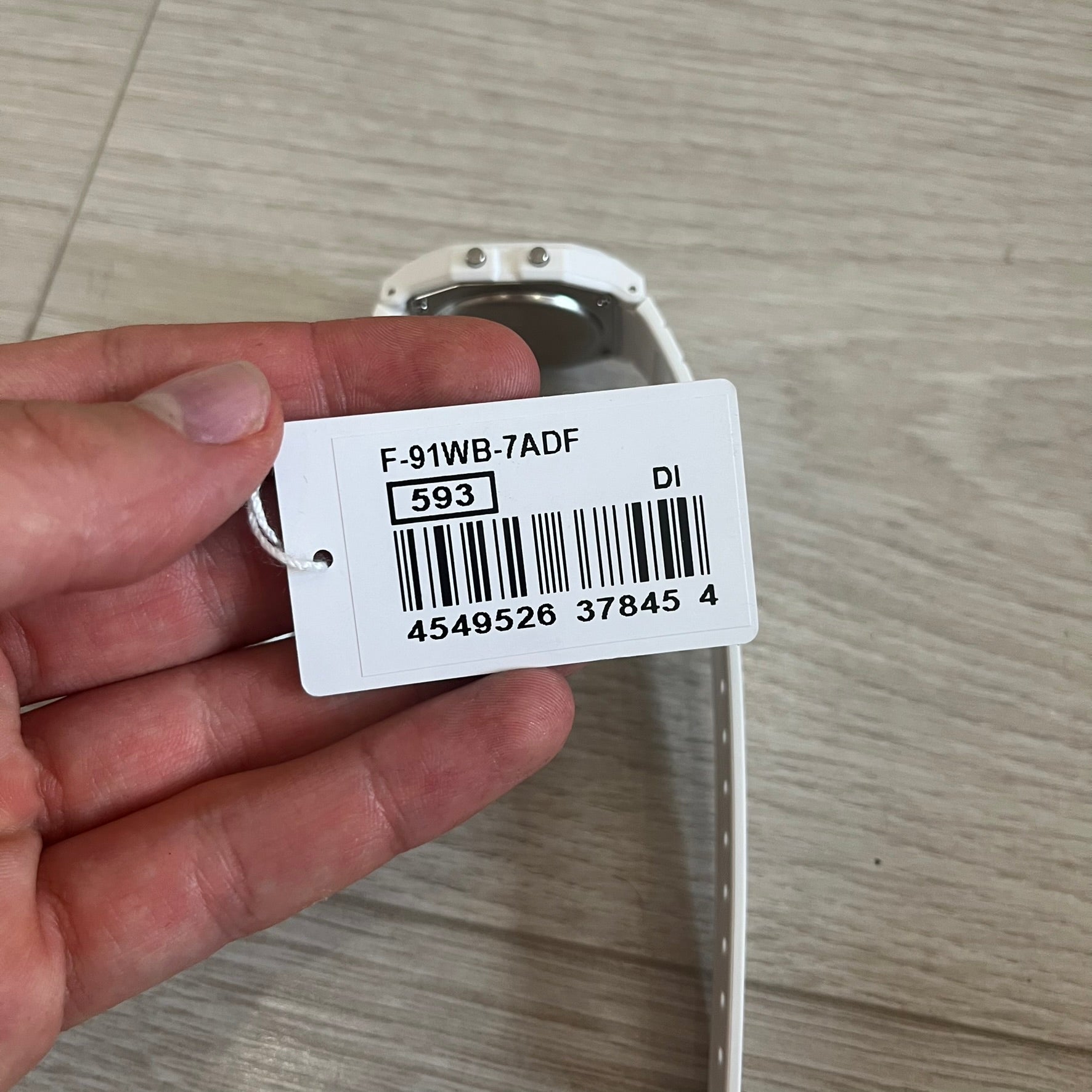 Hand holding a product tag with a barcode and text on a wooden surface