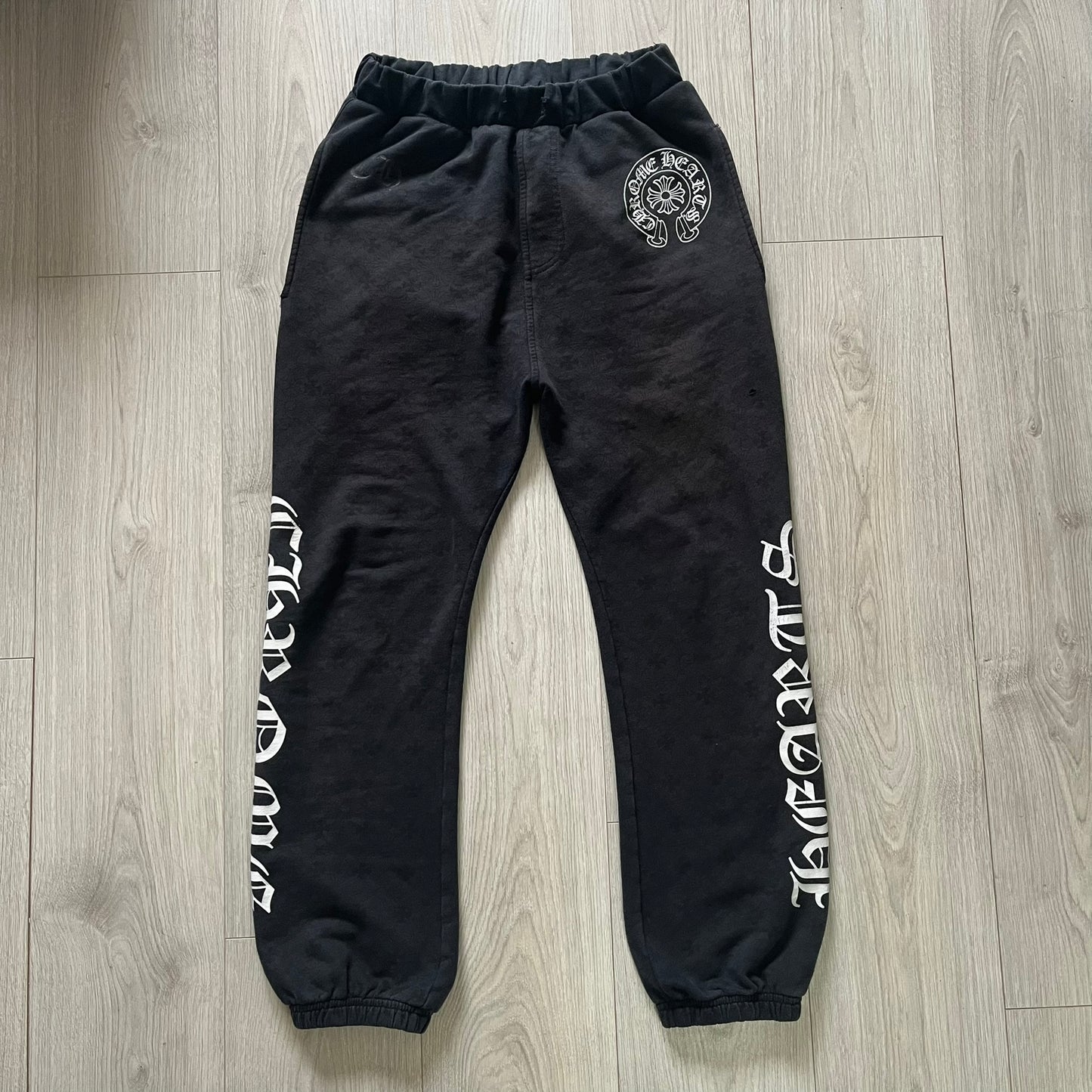 Black sweatpants with white text and a logo on a wooden floor