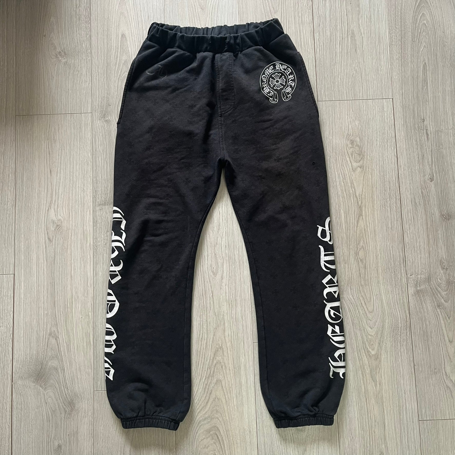 Black sweatpants with white text and a logo on a wooden floor