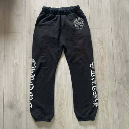 Black sweatpants with white text and a logo on a wooden floor
