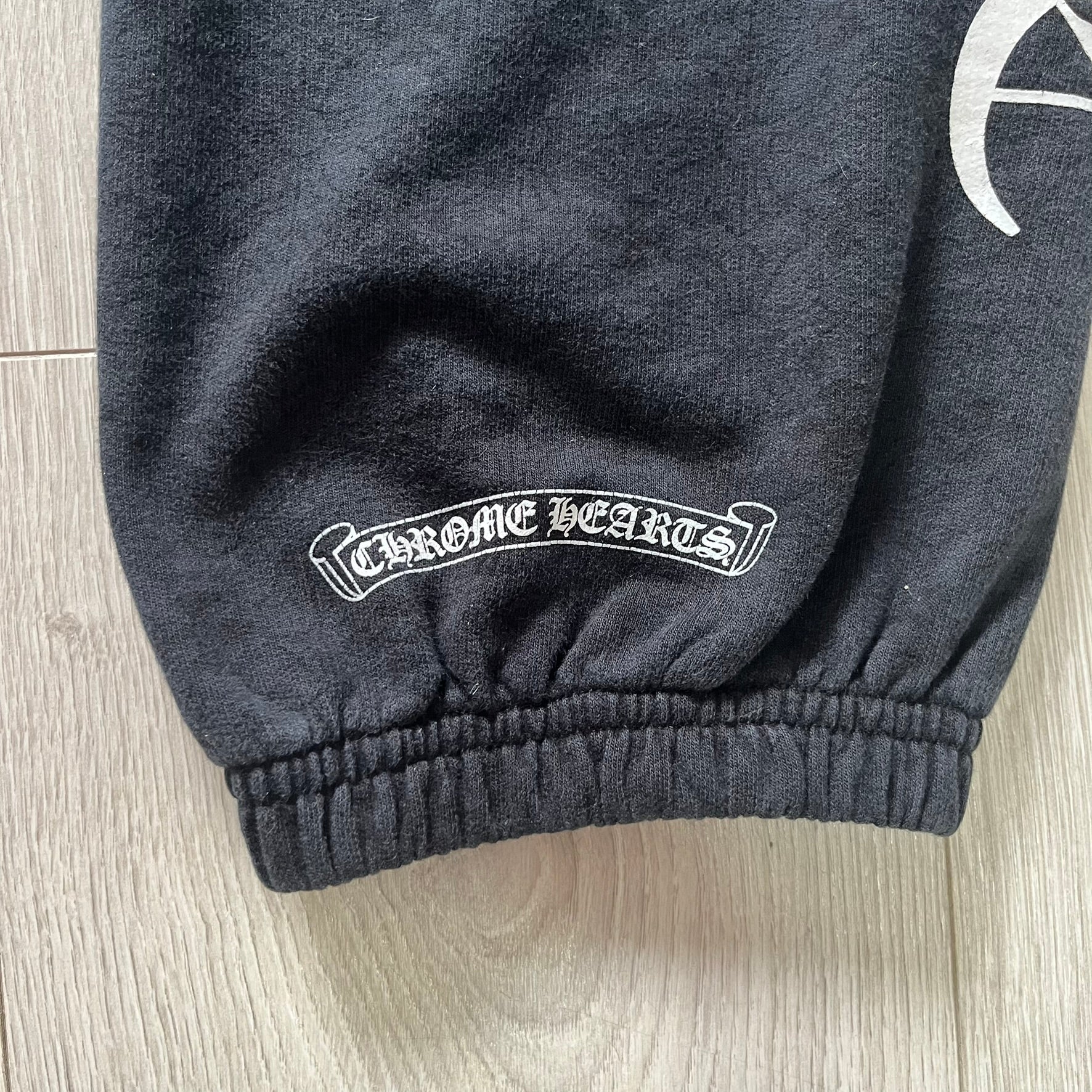 Dark gray sweatpants with 'Chrome Hearts' logo on a light wooden floor.