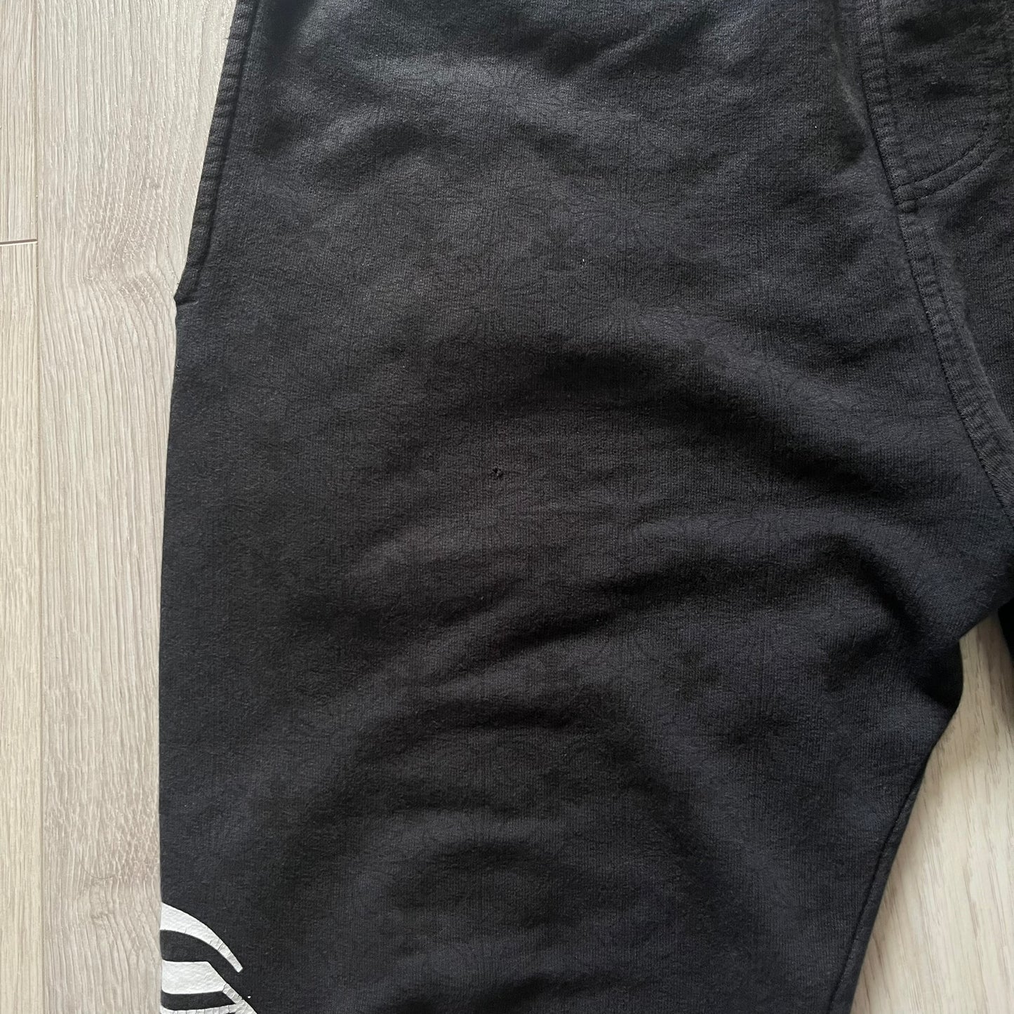 Close-up of black shorts with a brand logo on a wooden floor.