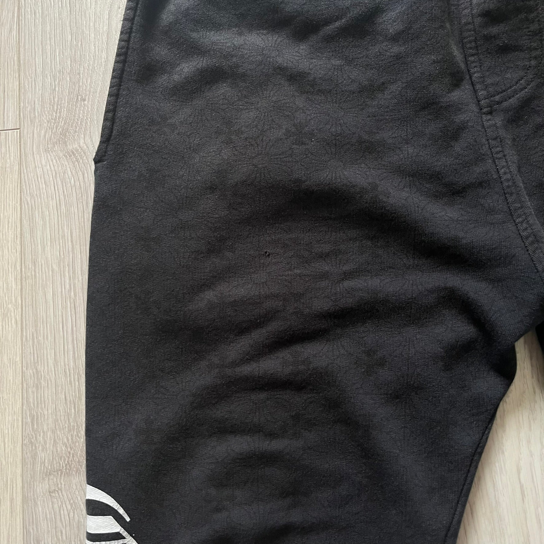 Close-up of black shorts with a brand logo on a wooden floor.