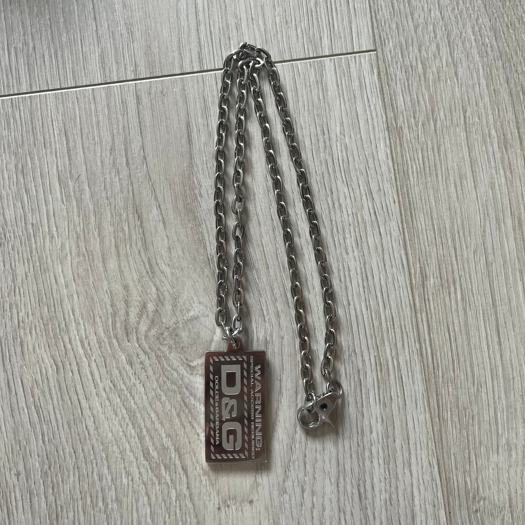 Silver chain with a rectangular tag on a wooden surface