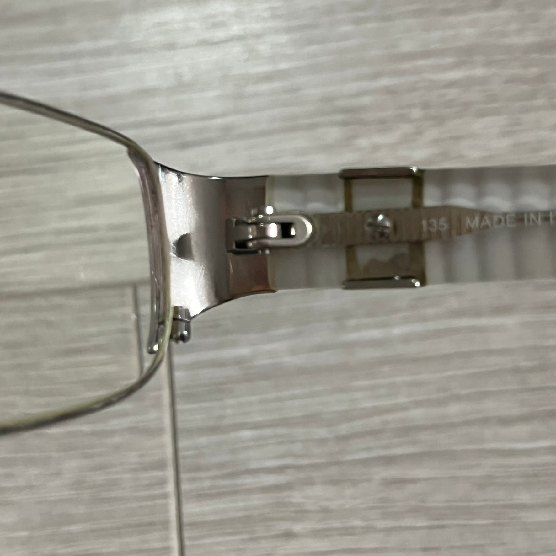 Close-up of a silver eyeglass frame on a textured gray background