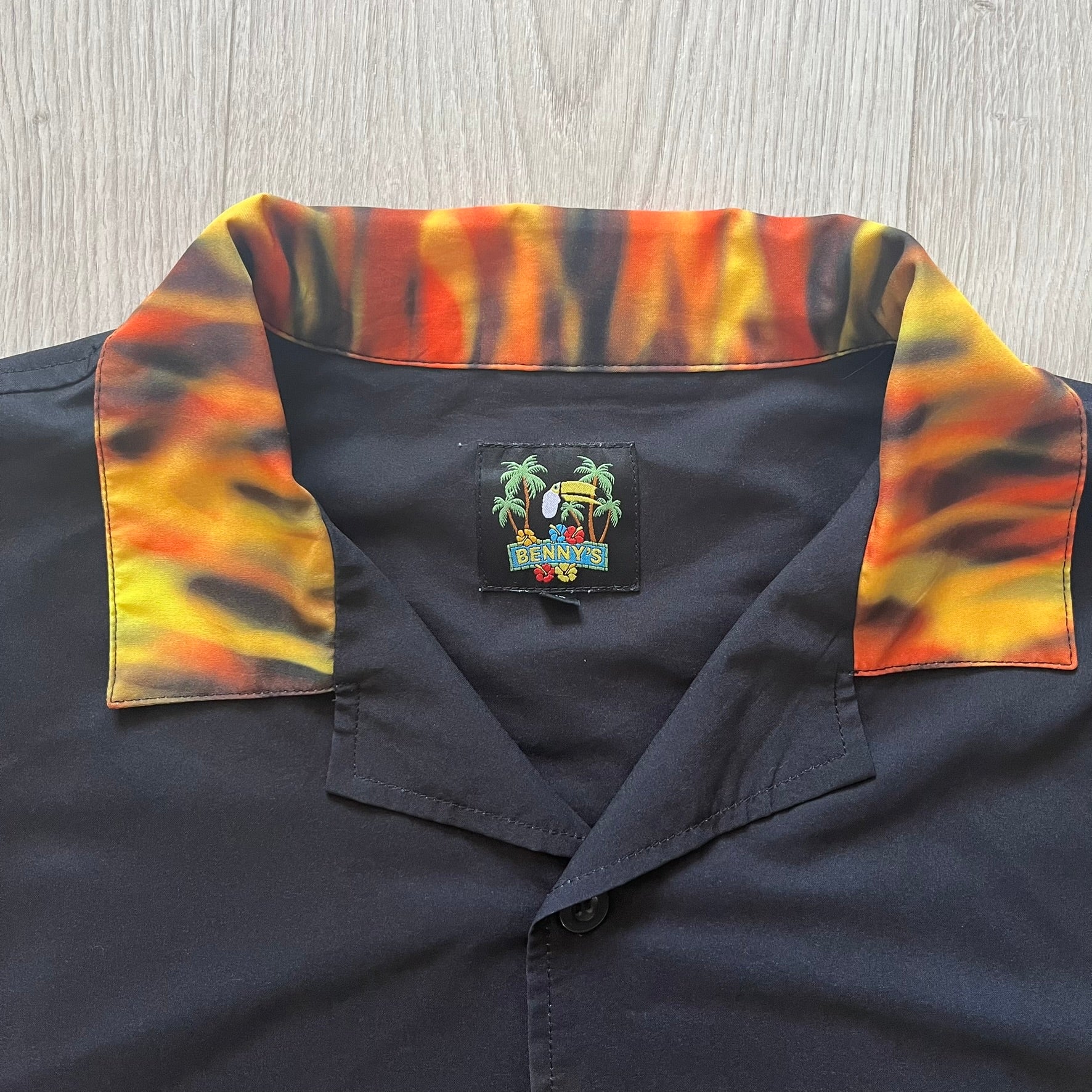 Black shirt with colorful collar and a brand logo on a wooden surface