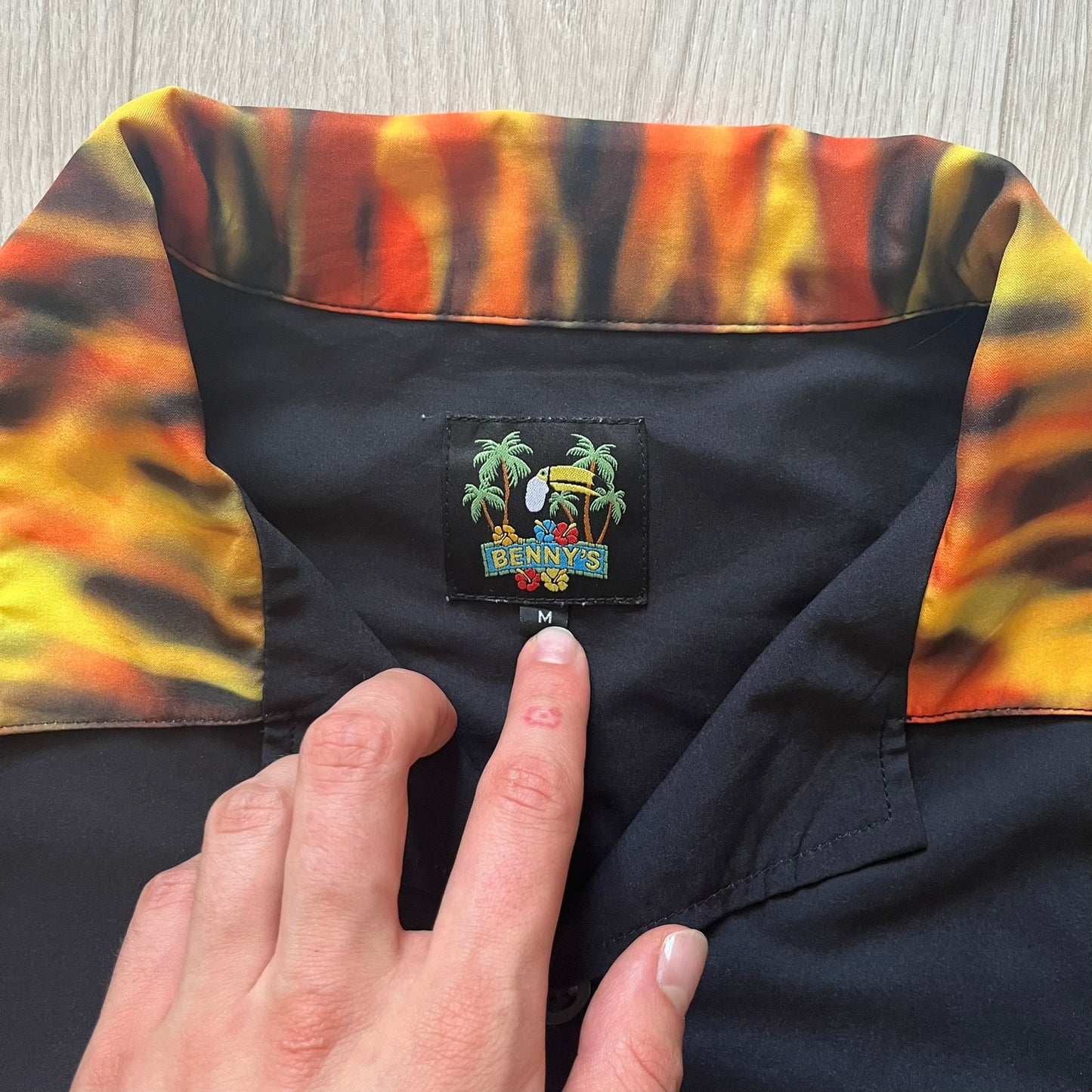 Close-up of a colorful shirt collar with a brand label, held by a hand.