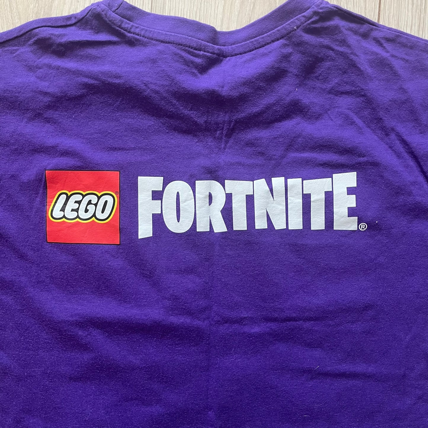 Purple t-shirt with LEGO Fortnite logo on a wooden surface