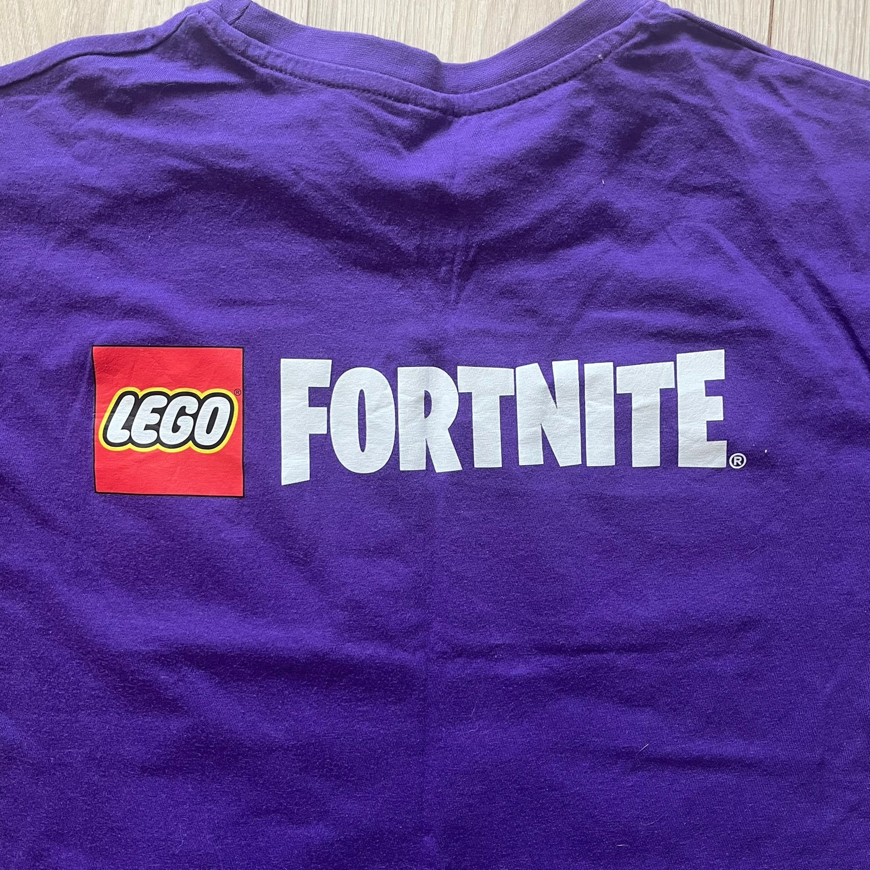Purple t-shirt with LEGO Fortnite logo on a wooden surface