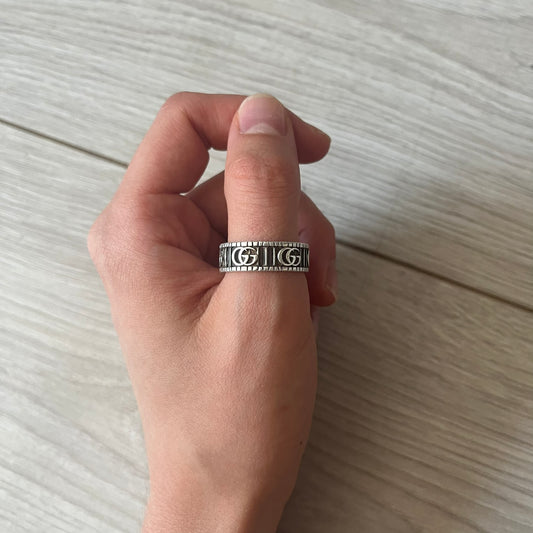 Hand wearing a silver ring with intricate designs on a light wooden surface