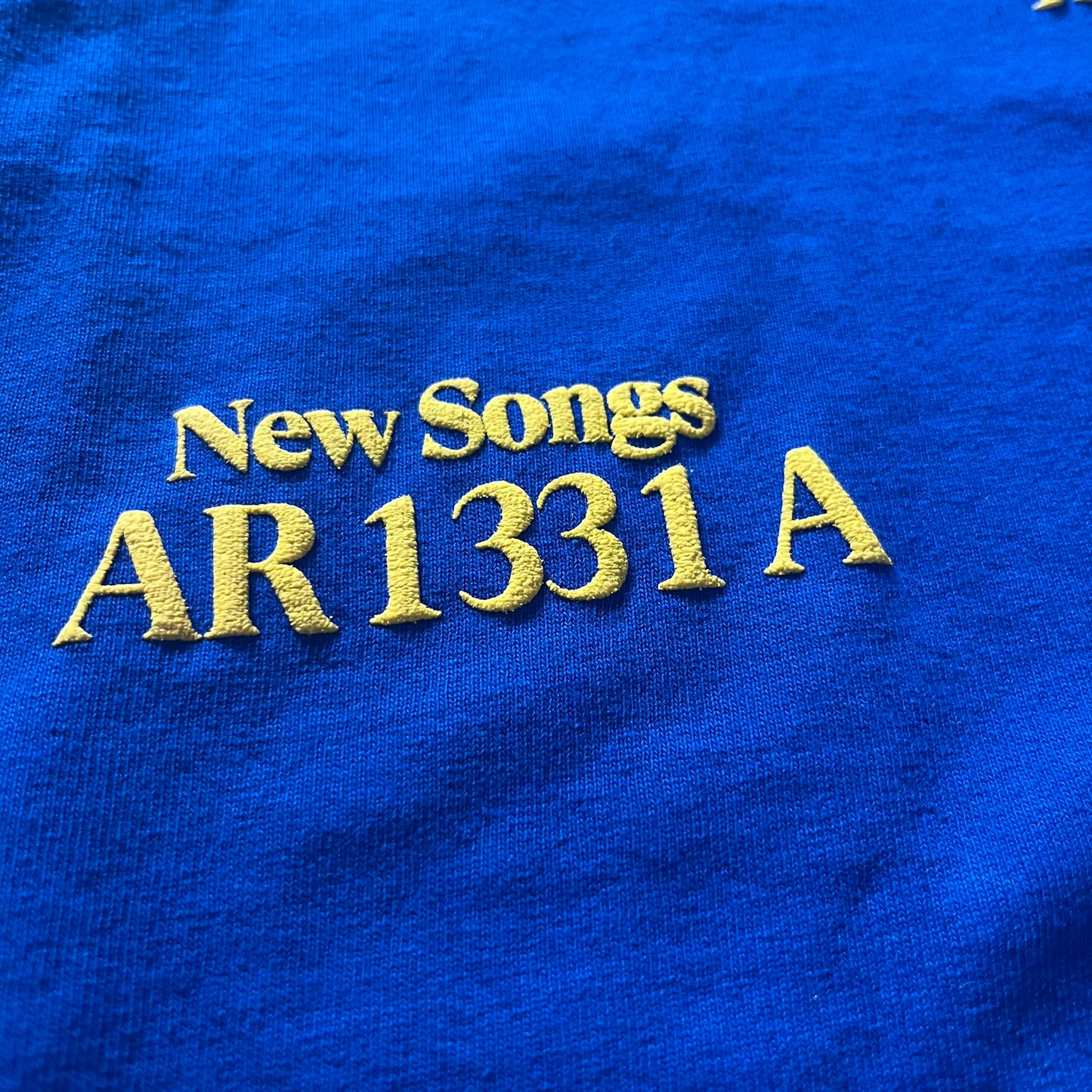 Blue fabric with embroidered text 'New Songs AR1331A' in yellow thread