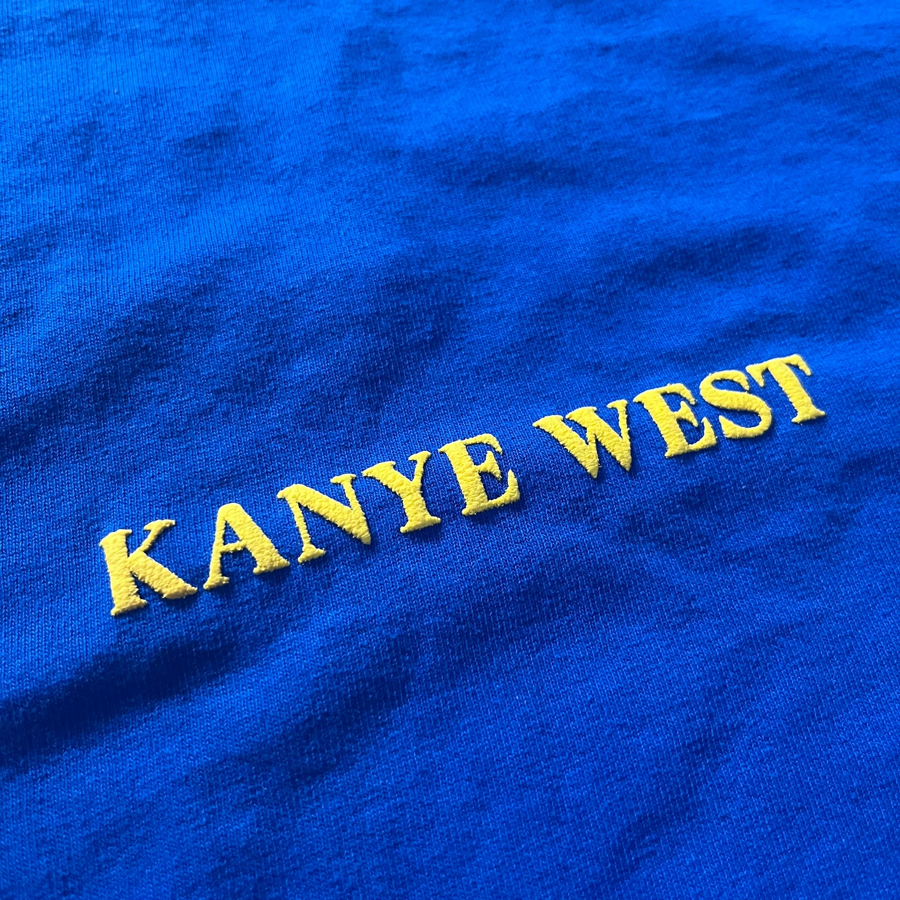 Blue fabric with 'Kanye West' embroidered in yellow