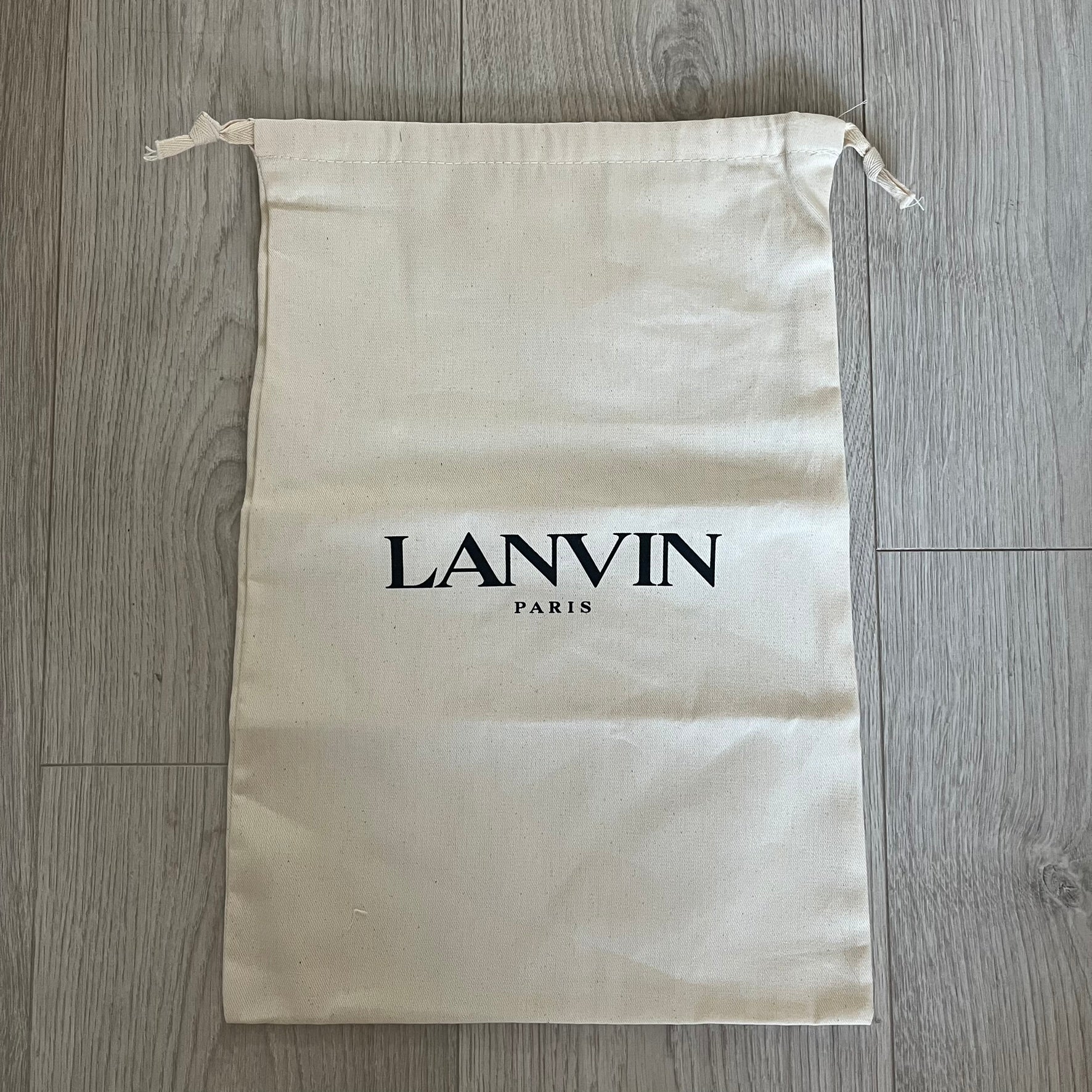 Beige drawstring bag with 'LANVIN PARIS' logo on a wooden floor.
