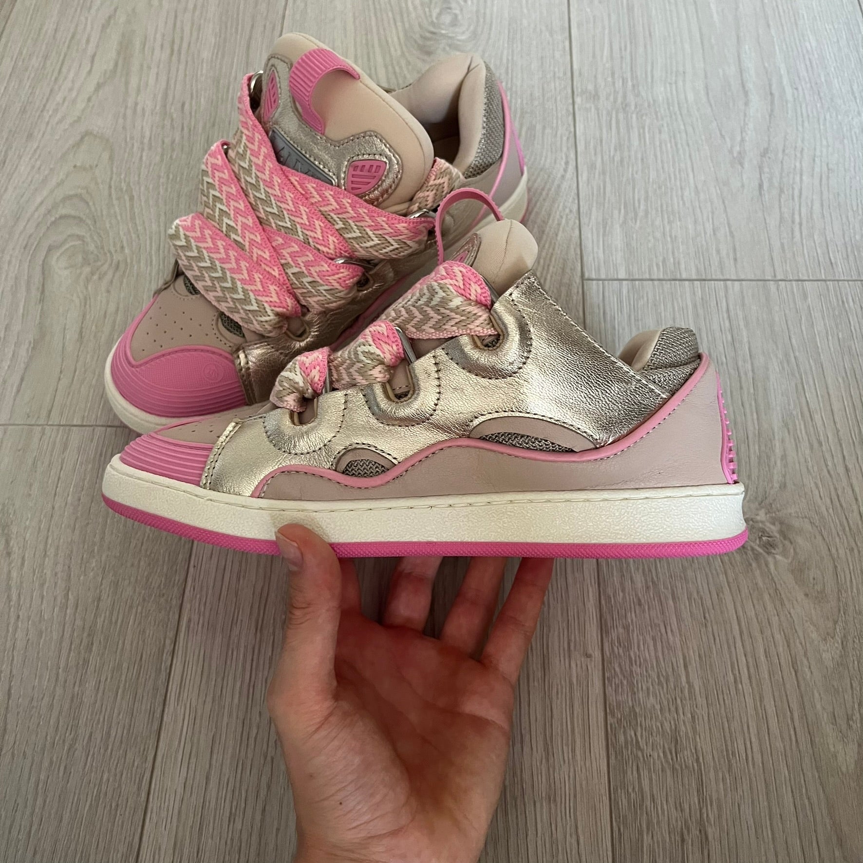 Pair of silver and pink sneakers held by a hand on a wooden floor.