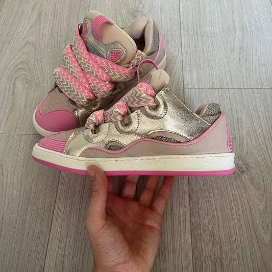 Pair of silver and pink sneakers held by a hand on a wooden floor.