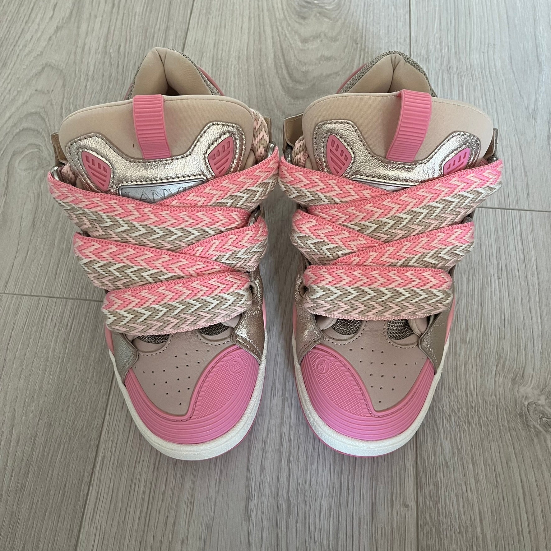 Pair of pink and beige sneakers with braided shoelaces on a wooden floor.