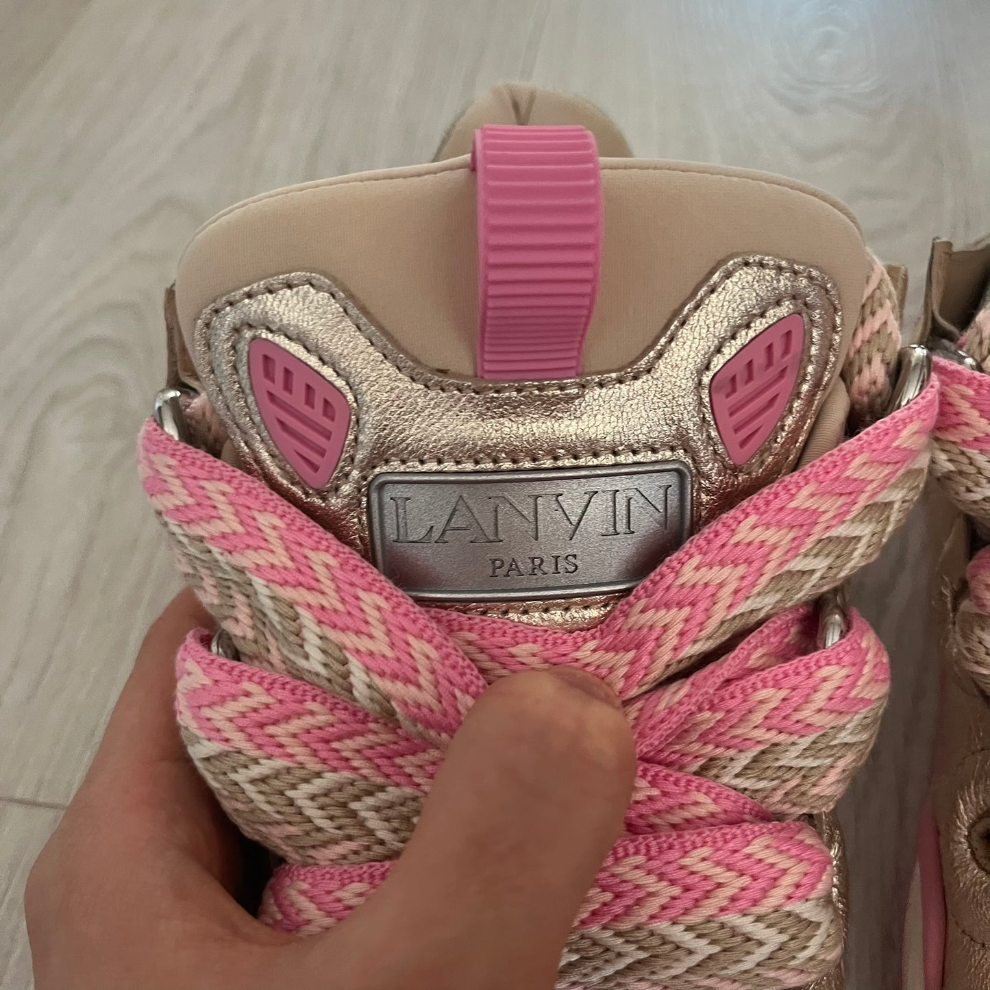 Pink and beige shoe with 'Lanvin' branding held by a hand on a light wooden floor.