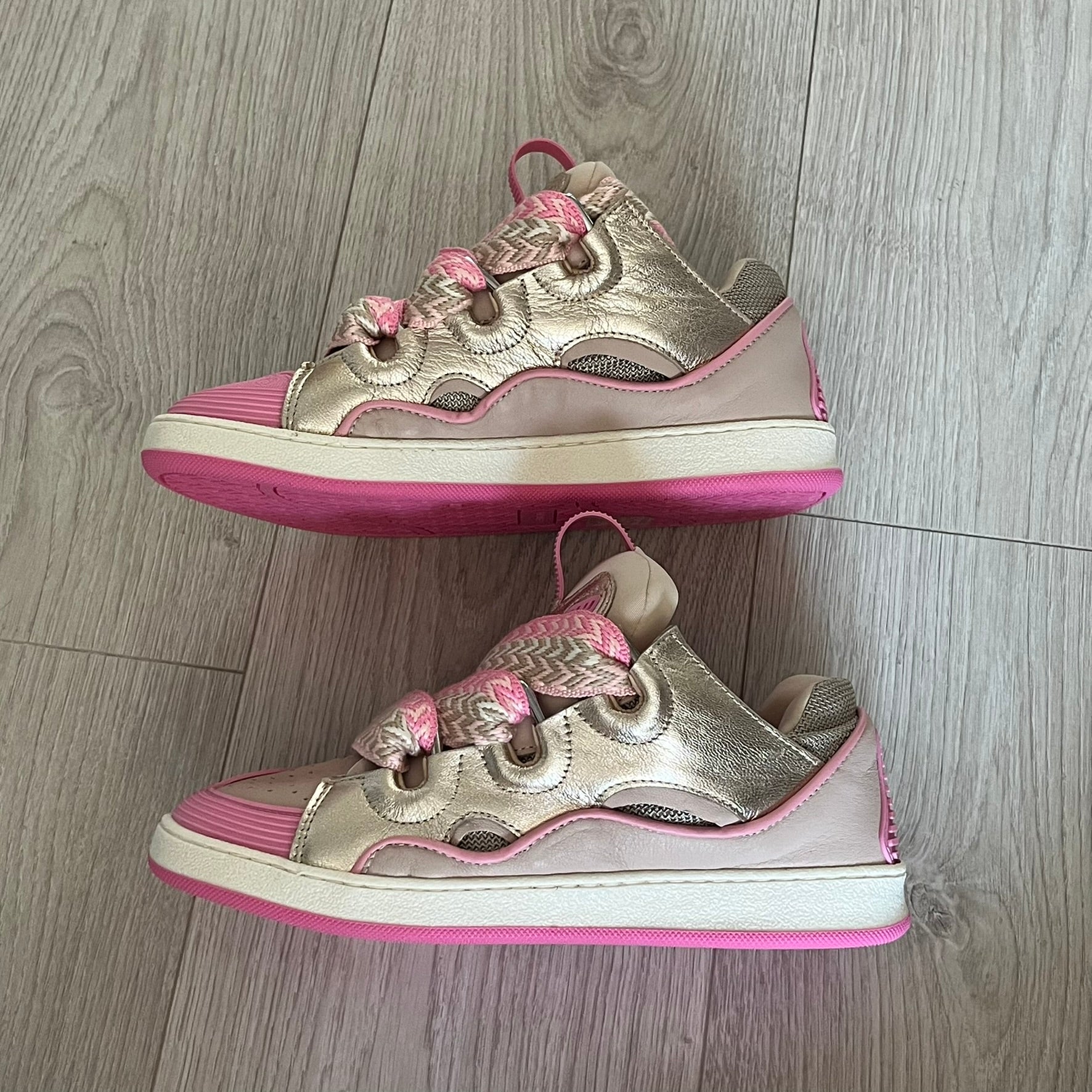 Pair of pink and gold sneakers on a wooden floor