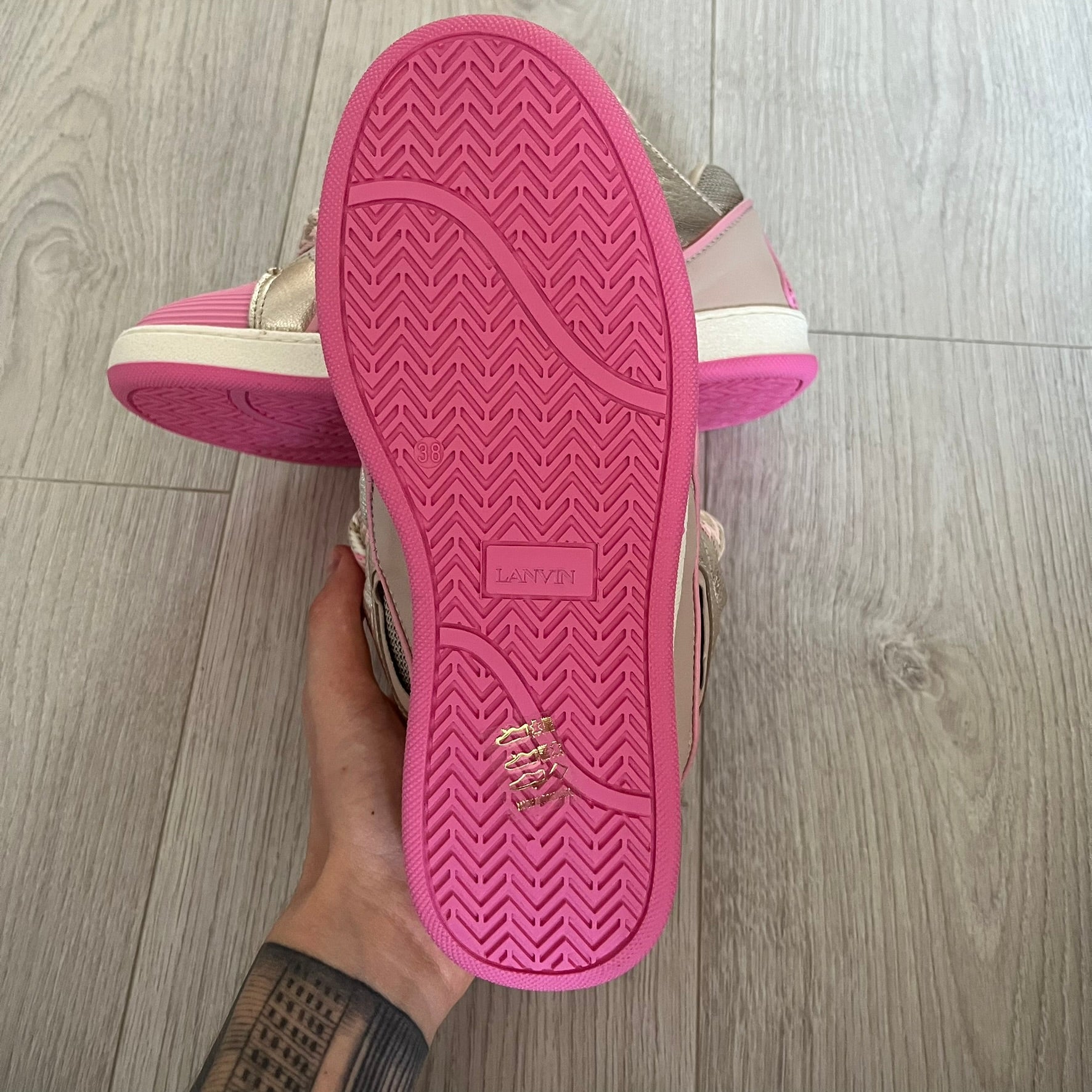 Pink sole of a shoe held by a hand on a wooden floor
